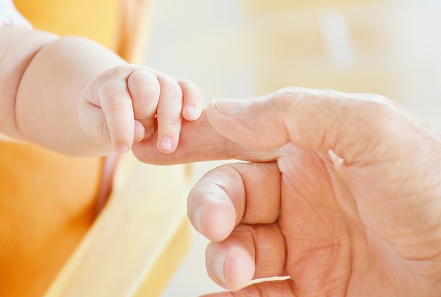 Image of an infant's fingers holding an adult's finger